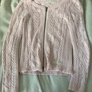 Ljusrosa kofta från Odd Molly - Supersöt ljusrosa kofta från Odd Molly med stickat mönster och dragkedja framtill. Koftan har långa ärmar, ribbade muddar och fina virkade detaljer. Perfekt för lager-på-lager och ger en romantisk vibe till din outfit.