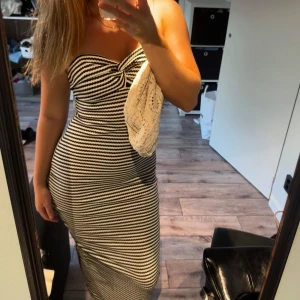 Randig axelbandslös långklänning - Säljer en snygg axelbandslös långklänning med svartvita ränder och twistad detalj vid bysten. Klänningen är figurnära och har en stilren, tidlös look som passar perfekt till sommaren. Materialet känns mjukt och stretchigt för en bekväm passform. Använd 2 gånger 