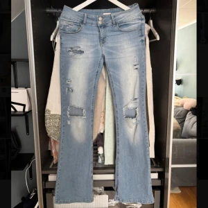 Ljusblå bootcut jeans med slitningar - Säljer ett par ljusblå jeans med bootcut passform och snygga slitningar framtill och på bakfickorna. Jeanden är låg midjade med storlek 38. Midjemått 38 innerbenslängd 82 ungefär💗