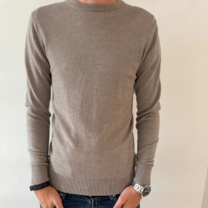 JOHN HENRIC MERINOULL TRÖJA  - Snygg beige stickad 100% merinoull tröja från John Henric med rund halsringning och långa ärmar. Perfekt för lager-på-lager och passar till både jeans och chinos. Tröjan har en klassisk, clean look och är tillverkad i mjukt material som känns skönt mot huden.