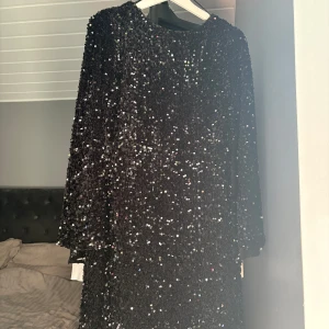 Svart paljettklänning från H&M - Glittrig svart kortklänning från H&M med paljetter över hela klänningen. Djup urringning i ryggen och långa ärmar. Perfekt för dig som vill sticka ut och glänsa på festen.🩷