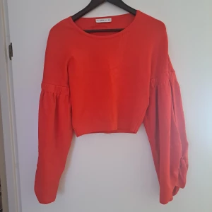 Röd croppad blus med puffärmar från Zara - Säljer en röd croppad blus från Zara med långa puffärmar och rund halsringning. Ärmarna har snygg rynkdetalj och blusen har en loose fit som ger en trendig siluett. Perfekt för dig som vill sticka ut med färg och volym.
