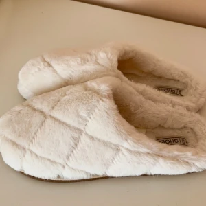 Vita fluffiga tofflor från NLY Shoes - Supermysiga vita tofflor från NLY Shoes med quiltad look och mjuk pälsimitation. Perfekta att glida runt i hemma när du vill ha det extra bekvämt. Sulan är mönstrad för bättre grepp och insidan är helt täckt av fluffigt material.