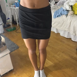 Svart tight kortkjol från Lindex - Enkel och stilren svart kortkjol från Lindex med tight passform. Kjolen har en bred midjeresår och är gjord i mjukt stretchigt material som sitter snyggt på kroppen. Perfekt att matcha med en crop top eller oversized hoodie.