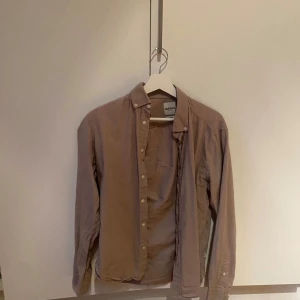 Beige linneskjorta dobber - Säljer en stilren beige skjorta från dobber med klassisk krage och knäppning framtill. Skjortan är långärmad och tillverkad i ett mjukt bomullstyg som känns skönt mot huden. Perfekt för dig som gillar en enkel och clean look. Storlek S