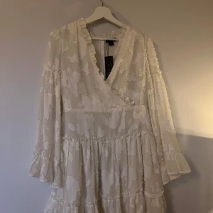 Vit omlottklänning med volang - Superfin vit omlottklänning från Boohoo med långärmade volangärmar och strukturmönster i tyget. Köpt som studentklänning men blev istället oanvänd, lapp finns kvar. 🤍