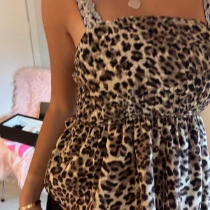 Leopardmönstrad blus med volang - Säljer en snygg leopardmönstrad blus med breda axelband och volangig nederdel. Toppen har en smockad midja som ger en fin form och är perfekt för dig som vill sticka ut. Mjuk och skön känsla, passar till både jeans och kjol.