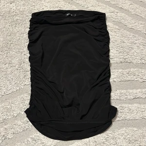 Svart tight kortkjol från NLY One - Svart tight kortkjol från NLY One med snygga rynkade sidor som ger en cool och trendig look. Kjolen har en enkel design och är perfekt att styla med en crop top eller oversized t-shirt. Materialet är stretchigt och följsamt.