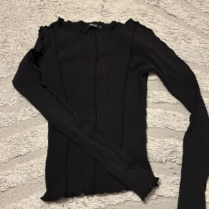 Svart ribbad långärmad topp från Bik Bok - Säljer en svart långärmad topp från Bik Bok med ribbad struktur och vågiga kanter vid hals, ärmslut och nederkant. Snygg passform och stretchigt material som sitter skönt på kroppen. Perfekt att styla med jeans eller kjol.