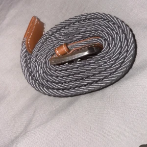 Grått flätat bälte med skinn-detaljer (revernite) - Jag säljer min killes revernite bälte pga att det inte används längre. Det är i mycket fint skick!