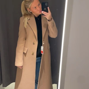 Beige lång kappa med knappar - Säljer en snygg beige kappa med klassisk krage och två knappar framtill. Modellen är lång och har fickor med lock på sidorna. Perfekt för dig som gillar stilrena och tidlösa plagg. Passar till jeans och sneakers eller boots. Köpt ifrån mango förra året men är tyvärr för liten iår! En favorit🤎
