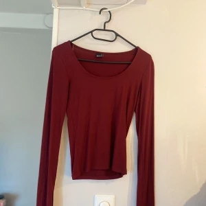 Vinröd långärmad topp Gina Tricot  - Vinröd långärmad topp från Gina Tricot i storlek XS. Modellen är figurnära med rund halsringning och har en liten slitsdetalj vid ärmsluten. Tunt och mjukt material som känns skönt mot huden. Perfekt att styla med jeans eller kjol.