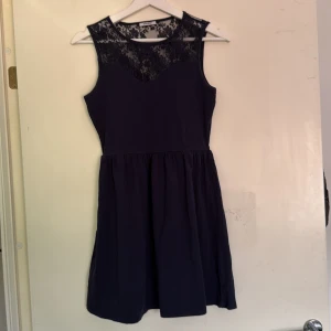 Mörkblå spetsklänning från ONLY - Supersöt mörkblå kortklänning från ONLY med ärmlös design och vacker spets upptill. Klänningen har rund halsringning och markerad midja som ger en snygg siluett. Perfekt för dig som gillar stilrena detaljer och romantisk känsla.