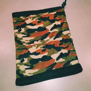 Camo fleecehalsduk med dragsko - Säljer en tubformad halsduk med camouflage-mönster i grönt, svart, beige och brunt. Insidan är mjuk och svart fleece, och halsduken har en praktisk dragsko upptill. Perfekt för kalla dagar när du vill ha både stil och värme.  Helt & fint skick