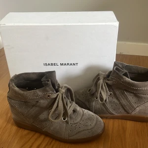 Beige mockasneakers Isabel Marant - Snygga beige sneakers från Isabel Marant i mjuk mocka med perforerade detaljer och snörning. Skorna har en diskret kilklack och gummisula, vilket ger en cool och sportig look. Perfekta till jeans eller kjol för en trendig vardagsstil.