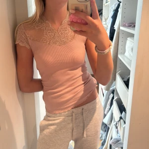 Ljusrosa ribbad topp med spets - Supersöt ljusrosa ribbad topp med spetsdetaljer över axlar och halsringning. Ärmlös modell med romantisk känsla och figurnära passform. Perfekt för dig som gillar feminina detaljer och en mjuk, skön känsla.