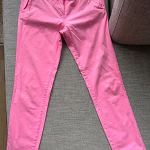 Maison Scotch rosa chinos - Snygga rosa chinos från Maison Scotch med klassisk passform och dragkedja. Byxorna har fickor fram och bak, bälteshällor och är tillverkade i mjuk bomull. Perfekta för dig som vill sticka ut med färg och ändå ha en clean look.