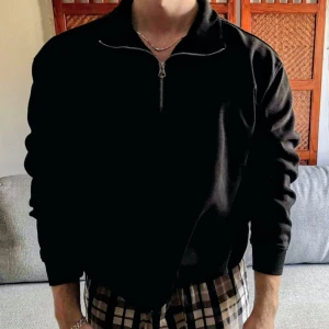 Svart half zip tröja från Weekday - Svart långärmad tröja från Weekday i mjuk bomullsmix. Klassisk och clean design med hög krage och silverfärgad half zip-dragkedja framtill. Perfekt för lager-på-lager och chill vardagsstil.