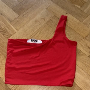 Röd one shoulder topp från Dynamic Mode - Snygg röd one shoulder topp från Dynamic Mode. Topp i stretchigt material med asymmetrisk axel och tight passform. Perfekt för dig som vill sticka ut med en enkel men cool look.