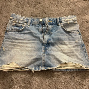 Ljusblå jeanskjol från Pull&Bear - Säljer en ljusblå jeanskjol från Pull&Bear i klassisk femficksmodell. Kjolen är kort och har slitna detaljer och fransad nederkant för en cool, avslappnad vibe. Perfekt till sneakers eller boots för en trendig look.