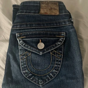 Low Waist bootcut True Religion jeans - Snygga blåa lågmidjade bootcut jeans från True Religion med deras ikoniska bakfickor.  Länge på byxorna är 96cm och har storlek W26. Säljer pga att den tyvärr är för stor för mig. Hör gärna av dig för frågor, priset kan diskuteras vid snabbköp❤️❤️