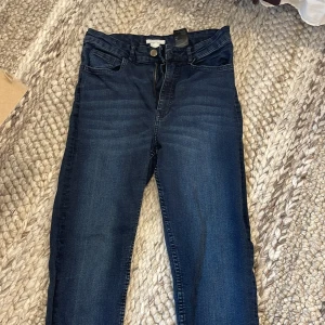 Mörkblå skinny jeans från H&M, stl 40 - Mörkblå skinny jeans från H&M i storlek 40. Jeansen har klassisk femficksdesign, hög midja och smal passform hela vägen ner. Materialet är stretchigt för extra komfort och de har snygga slitningar framtill för en cool look.