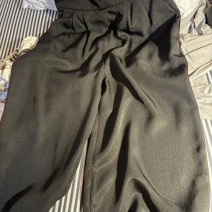 Svarta vida kostymbyxor - Snygga svarta kostymbyxor och vida ben. Byxorna har en elegant och flowy känsla, perfekta för en clean och stilren look. Materialet är slätt och ger en dressad vibe. Passar dig som gillar trendiga och bekväma byxor med mycket rörelse.
