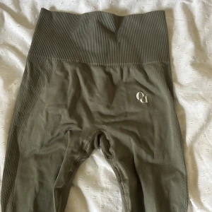 Olivgröna seamless leggings från Hanna Öbergs märke - Oanvända Snygga olivgröna seamless leggings från Hanna Öbergs märke  med hög midja och ribbad linning. Materialet är stretchigt och bekvämt, perfekt för träning eller chill. Diskret Aim'n-logga på ena benet och scrunch-detalj bak för extra passform.