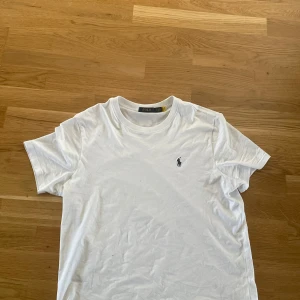 Vit t-shirt från Polo Ralph Lauren, strl, M/L - Klassisk vit t-shirt från Polo Ralph Lauren med rund hals och broderad logga på bröstet. Skön passform och tillverkad i mjuk bomull. Perfekt till jeans eller shorts för en clean och stilren look.