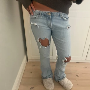 Ljusblå ripped bootcut jeans - Säljer ett par ljusblå jeans och slitningar vid knäna. Jeansen har låg midja, klassisk femficksmodell och råa kanter nertill. Perfekta för en avslappnad och trendig look. Fint skick bortsett från att de är lite söndertrampade längst ner, vilket jag dock tycker är en fin detalj 💗