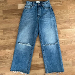 Abrand Jeans wide ripped jeans blå - Snygga blå jeans från Abrand Jeans, modell A Carrie Jean. De är högmidjade med raka, vida ben och har slitna detaljer vid knäna samt råa, fransiga benslut. 