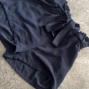 Mörkblå shorts med knytband från Only - Säljer ett par mörkblå shorts från Only med hög midja och knytband i midjan. Shortsen har en lös passform och resår i midjan för extra komfort. Perfekta för varma dagar och enkla att matcha med olika toppar.