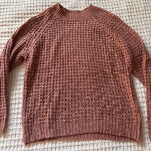 Rosa stickad tröja från 157 - Mysig rosa stickad tröja från 157 med grovstickat rutmönster. Tröjan har rund halsringning och långa ärmar. Perfekt för lager-på-lager och passar till både jeans och kjol.