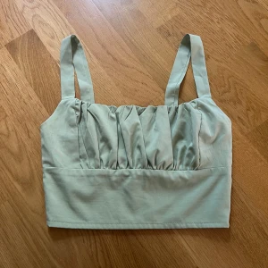 Ljusgrön croppad linnetopp från SHEIN - Säljer en ljusgrön croppad linnetopp från SHEIN i storlek XS. Toppen har breda axelband, rynkade detaljer framtill och smockad rygg för extra komfort. Perfekt till sommaren och enkel att matcha med jeans eller kjol.