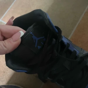 Svarta och blå Nike Air Jordans - Säljer ett par klassiska Nike Air Jordans i svart och blått. Skorna har snörning, rund tå och platt sula. Ikonisk Air Jordan-logga på sidan och Nike-märke på plösen. Perfekta för dig som gillar streetwear och sneakers med attityd.