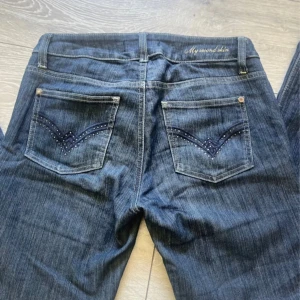 Mörkblå jeansbyxor från Gina Tricot - Säljer ett par mörkblå jeans från Gina Tricot med snygga detaljer på bakfickorna och broderad text 'My second skin' vid linningen. Klassisk femficksmodell med raka ben och normal passform. Perfekta till vardags!