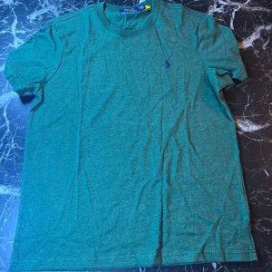 Grön t-shirt från Polo Ralph Lauren - Säljer en grön t-shirt från Polo Ralph Lauren med klassisk passform och liten broderad logga på bröstet. T-shirten har rund halsringning och är tillverkad i mjuk bomull. Perfekt för en avslappnad stil.