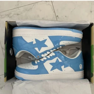 Blå och vita sneakers med stjärndetalj - Säljer ett par riktigt snygga sneakers i blått och vitt med en ikonisk stjärndetalj på sidan. Skorna har vit sula, vita skosnören och perforerad tå för extra ventilation. Perfekta för dig som vill sticka ut med din stil.