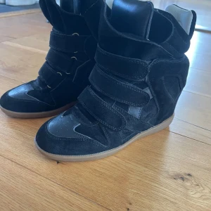 Svarta sneakers med kardborreband - Säljer ett par svarta sneakers med högt skaft och flera breda kardborreband. Skorna har en sportig design med rund tå och platt sula. Ovandelen är i mocka och syntet, och sulan är ljusbrun. Perfekta för dig som gillar streetstyle. Skorna är använda 2-4 gånger och är i princip i nytt skick. Storlek 37.