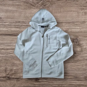 Vit hoodie från Sail Racing - Säljer en stilren vit hoodie från Sail Racing med dragkedja och broderad logga på bröstet. Tröjan har långa ärmar och en praktisk huva. Perfekt för en avslappnad stil. Tröjan är helt ny och endast använd fåtal gånger inomhus. Den har heller inga defekter och är självklart 100% äkta. Nypris: 1500, mitt pris: 750! Mer bilder kan fixas via DM. 