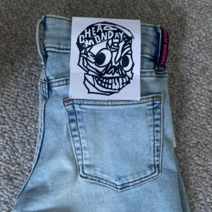 Ljusblå jeansbyxor från Cheap Monday - Säljer ett par ljusblå jeansbyxor från Cheap Monday (weekday) med slitna detaljer framtill. Byxorna har låg midja och är tillverkade i stretch-material. Aldrig använda, hittar inget kvitto