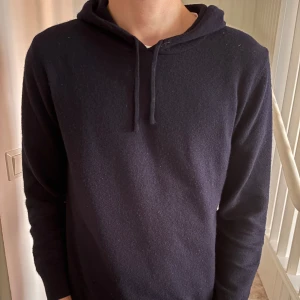 Kashmir tröja sayless - En stilren mörkblå hoodie med långa ärmar och dragsko i huvan. Tröjan är tillverkad i ett mjukt ullmaterial och passar perfekt till en avslappnad look. Enkel design utan tryck eller mönster. Modellen 182
