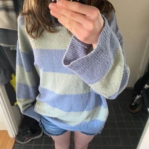 Randig stickad tröja från 157 - Mysig stickad tröja från 157 i ljusblått och ljusgrönt med breda ränder. Tröjan har lång ärm, rund halsringning och avslappnad passform. Nopprig men annars i bra skick. Väldigt oversized för att vara en M.