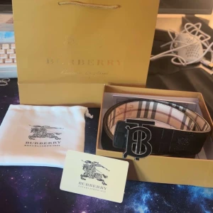 Svart skärp från Burberry med B-spänne - Säljer ett svart skärp från Burberry med stort B-spänne i metall. Skärpet har klassiskt rutigt mönster på insidan och är gjort i skinn. Kommer med originalpåse och förpackning.