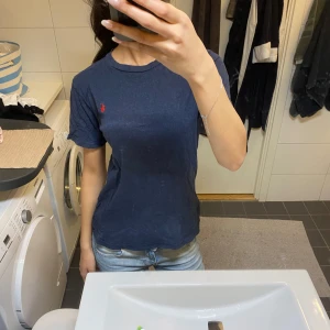 Marinblå t-shirt från Ralph Lauren - En klassisk marinblå t-shirt från Ralph Lauren med röd broderad logga på bröstet. T-shirten är kortärmad, har rund hals och är gjord i mjuk bomull. Perfekt till jeans för en clean och enkel look.