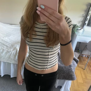 Randig ribbad croppad topp - Superfin croppad topp med svarta ränder på vit botten. Ribbad struktur och vågiga kanter vid ärmslut och nederkant. Kortärmad och figurnära passform, perfekt till jeans eller kjol. Enkel men ändå trendig stil.