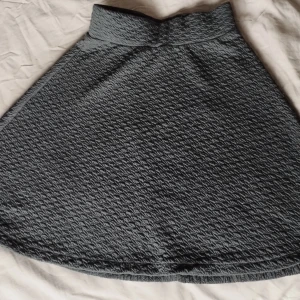 Svart kjol från Jyothi med sturktur/textur - Svart kjol från Jyothi med snygg struktur i tyget som ger en cool känsla. Kjolen har hög midja och en lätt utställd form som ger en fin siluett. Perfekt att styla med en stickad tröja eller en crop top för en trendig look.