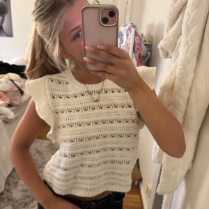 Vit stickad croppad topp med volang - Superfin vit stickad topp med korta volangärmar och snyggt hålmönster. Croppad modell som ger en fräsch och somrig vibe. Perfekt till jeans eller kjol för en chill look.