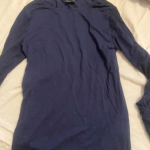 Mörkblå långärmad topp från Gina Tricot - En enkel och stilren mörkblå långärmad topp från Gina Tricot. Modellen är figurnära och passar perfekt till både jeans och kjol. Tillverkad i mjukt bomullsmaterial för en bekväm känsla hela dagen. Längst ut på ärmarna går de ut.