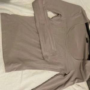 Beige långärmad topp från Gina Tricot - Säljer en beige långärmad topp från Gina Tricot med rundad, djup ringning. Toppen är i mjukt bomullsmaterial och har en enkel, stilren design som passar till många olika outfits. Vid ärmarna går de ut längst ner 